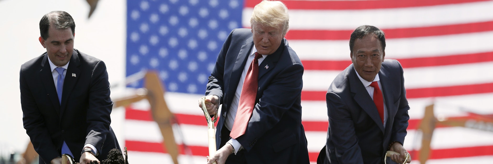 Donald Trump schippt werbewirksam: 2018 war er beim Baubeginn einer Fabrik in Wisconsin dabei, wo das taiwanesische Elektronik-Unternehmen Foxconn 13.000 Menschen beschäftigen wollte. Das Werk ist allerdings bis heute nicht fertig.