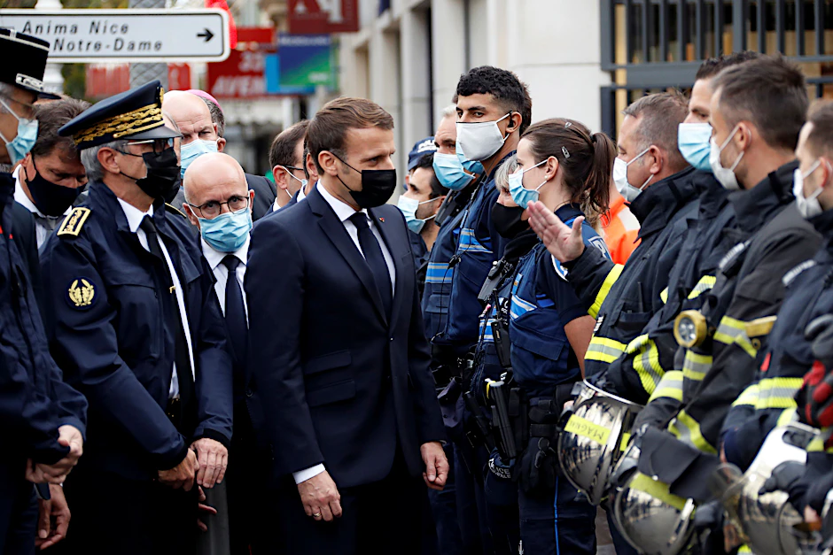 Emmanuel Macron (M.), Präsident von Frankreich, spricht nach einer Messerattacke in der Kirche Notre-Dame in Nizza mit Polizeibeamten. Bei dem Attentat hat es mindestens drei Tote und mehrere Verletzte gegeben.