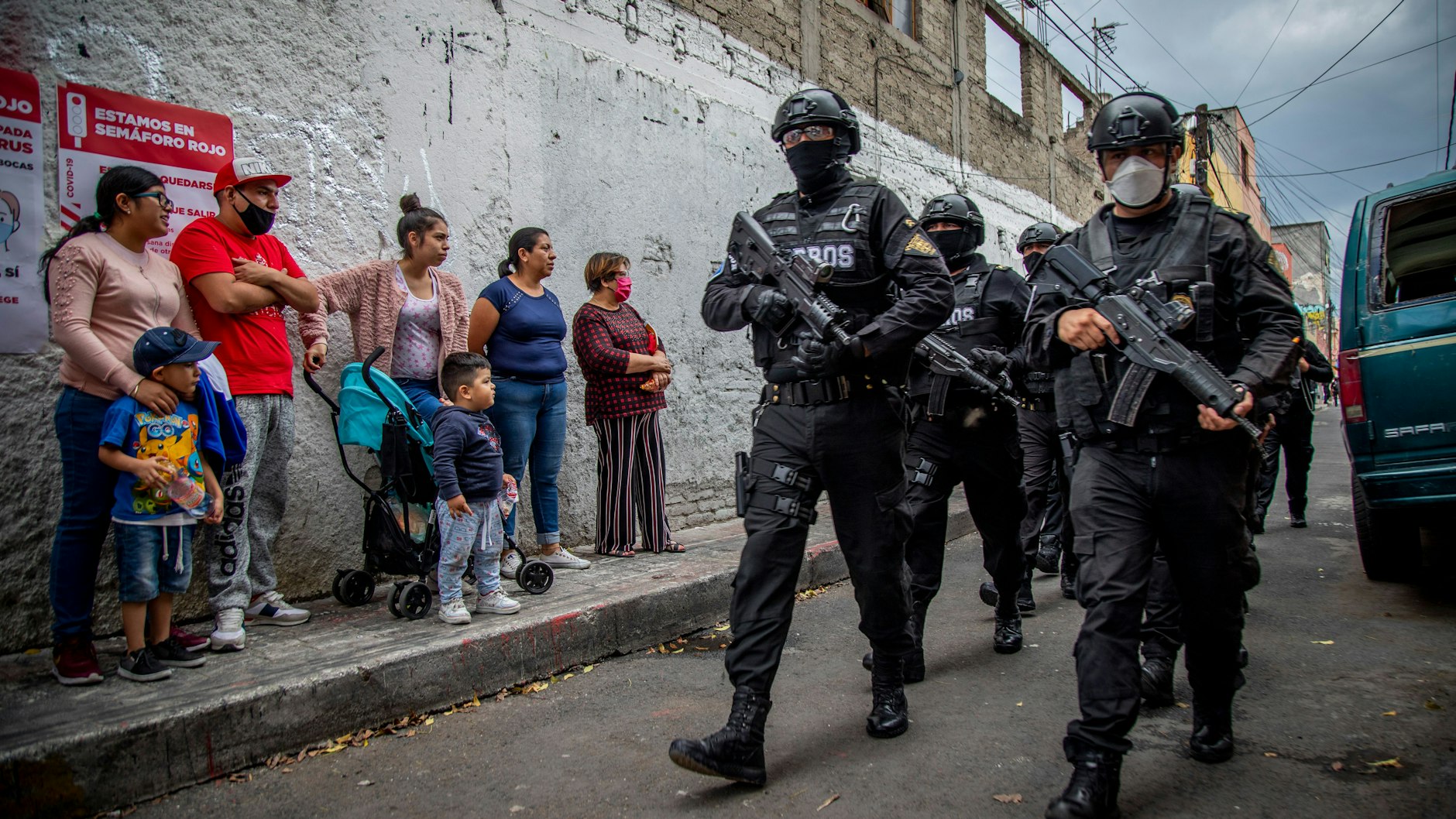 Frauen und Kinder schauen auf bewaffnete Polizisten mit Masken, die in Mexiko-Stadt den Drogenhandel bekämpfen.