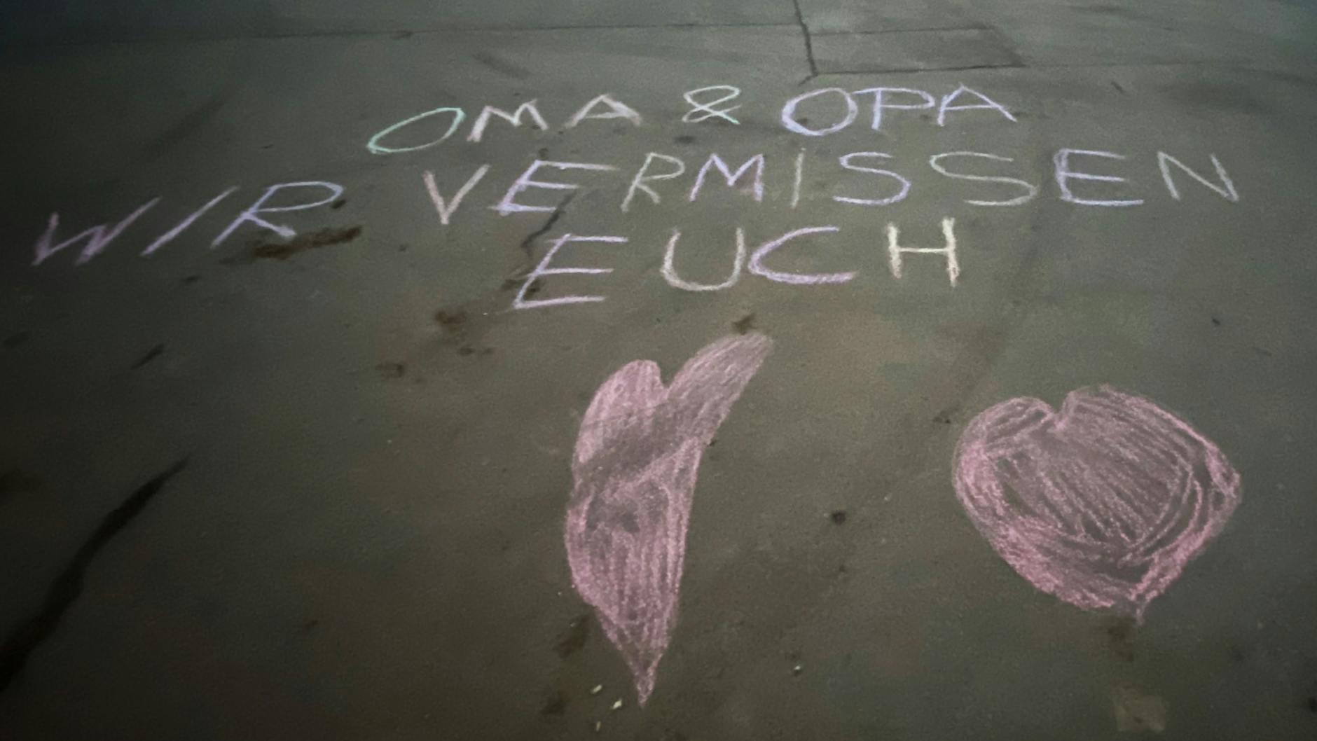 "Oma und Opa wir vermissen euch" steht auf einer Straße mit Kreide geschrieben vor einem Wohnhaus in Steglitz. 