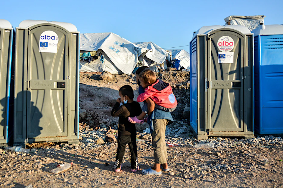 Kinder zwischen einer Reihe von Toilettenboxen im Flüchtlingscamp Kara Tepe