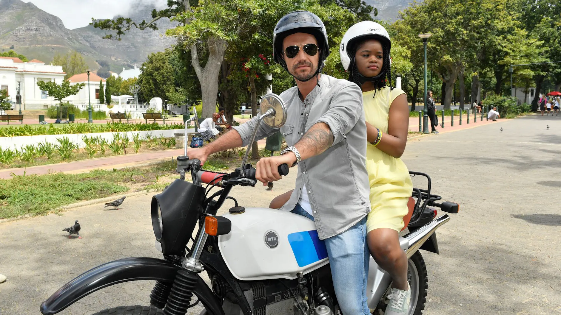Kapitän Max Parger (Florian Silbereisen) und Lea Bremer (Melodie Wakivuamina) sitzen auf einem Motorrad - Szene aus "Das Traumschiff: Kapstadt". 