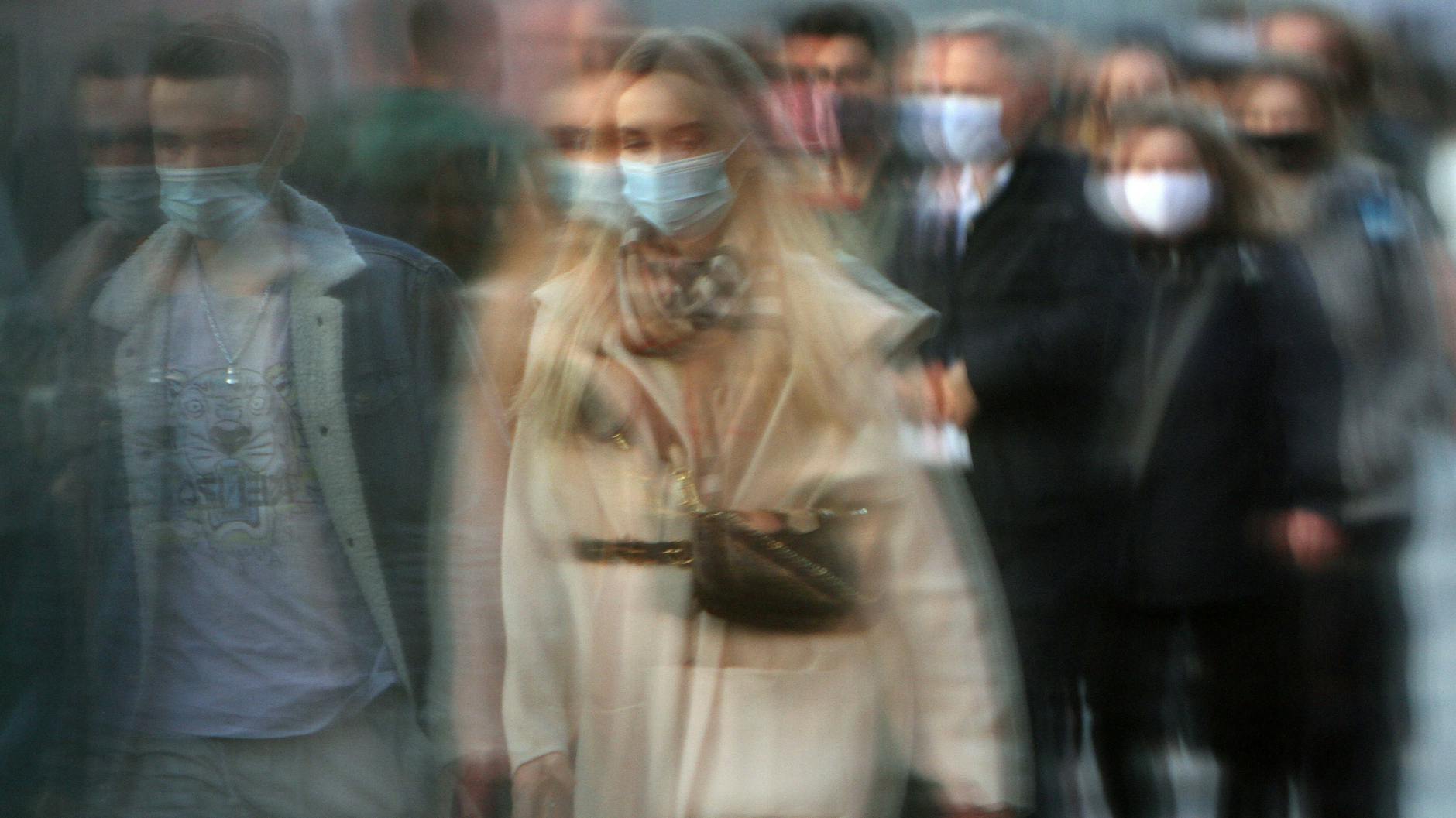 Passanten mit Mund- und Nasenbedeckung spiegeln sich in einer Schaufensterscheibe.