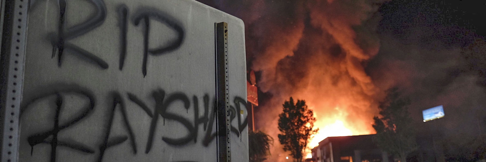 „RIP Rayshard“ steht auf einem Schild, während im Hintergrund ein Restaurant brennt.