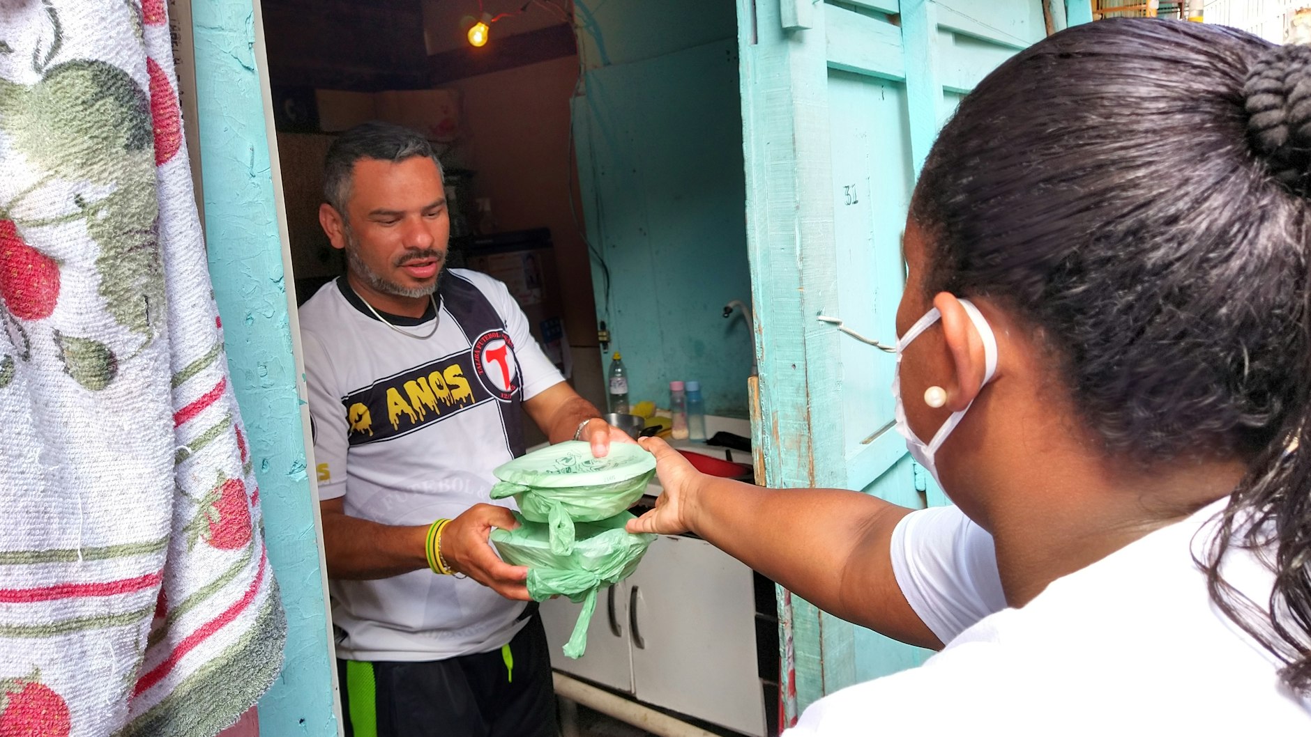 Laryssa da Silva reicht einem Mann zwei Essenspakete in die Wohnung.