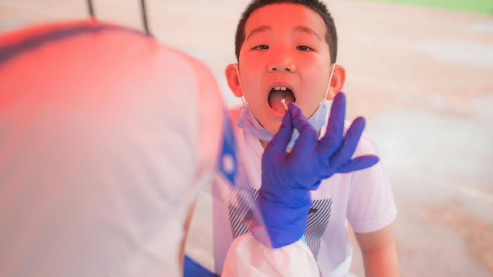 Ein Mitarbeiter des Gesundheitswesen entnimmt eine Rachenprobe für einen Corona-Test bei einem Jungen. (Symbolbild)