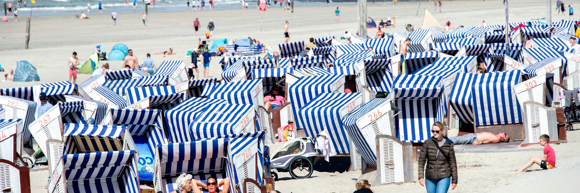 Urlaubsgäste bräunen sich auf der Insel Norderney in ihren Strandkörben, eine Spaziergängerin trägt noch eine Daunenjacke: Dieser Sommer zeigt sich sehr durchwachsen.