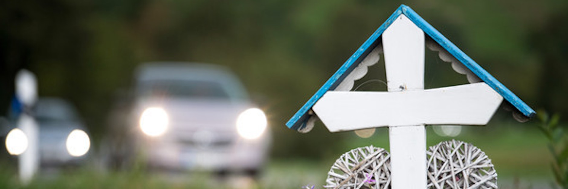 Autos fahren an einem weißen Kreuz für eine Unfalltote vorbei.