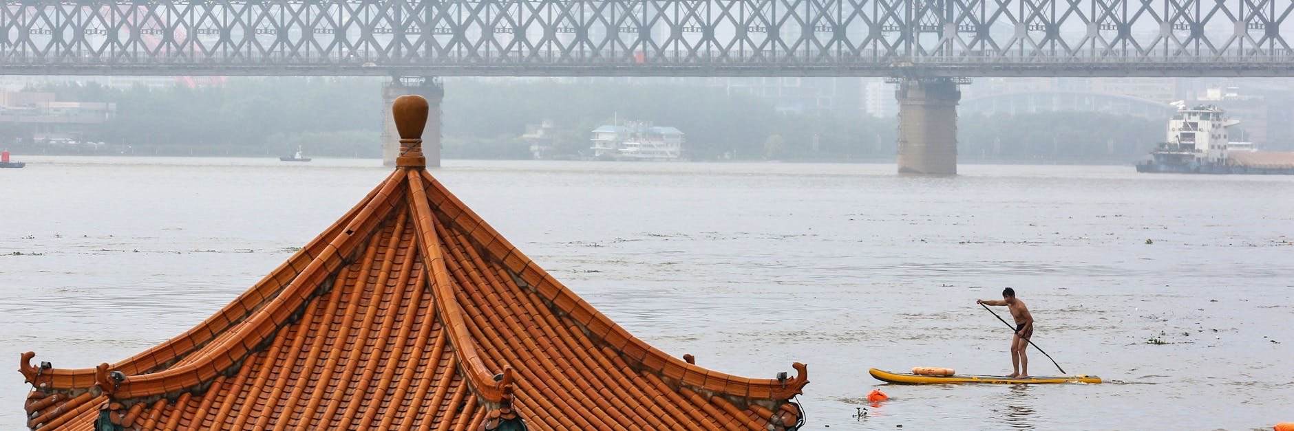 TOPSHOT - People (foreground) swim in the swollen Yangtze River as the roof of an inundated pavilion is seen above floodwaters in Wuhan in China's central Hubei province on July 8, 2020. (Photo by STR / AFP) / China OUT