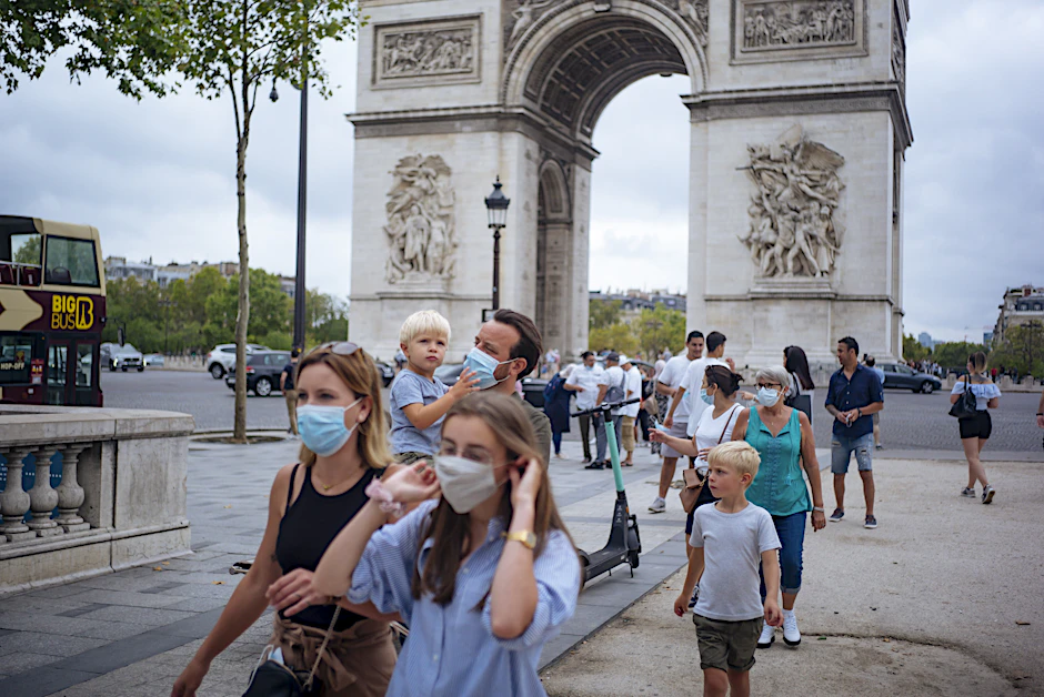 Touristen mit Schutzmasken spazieren auf der Prachtstraße Champs-Elysees.