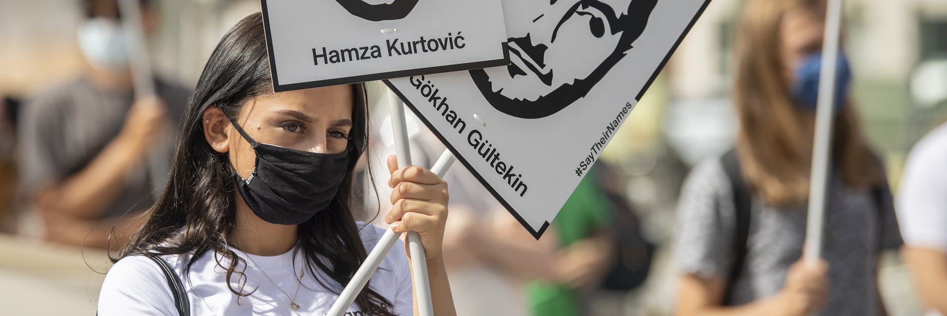 Eine Frau hält bei der offiziellen Gedenkveranstaltung Schilder mit den Fotos von zwei Opfern in den Händen. 