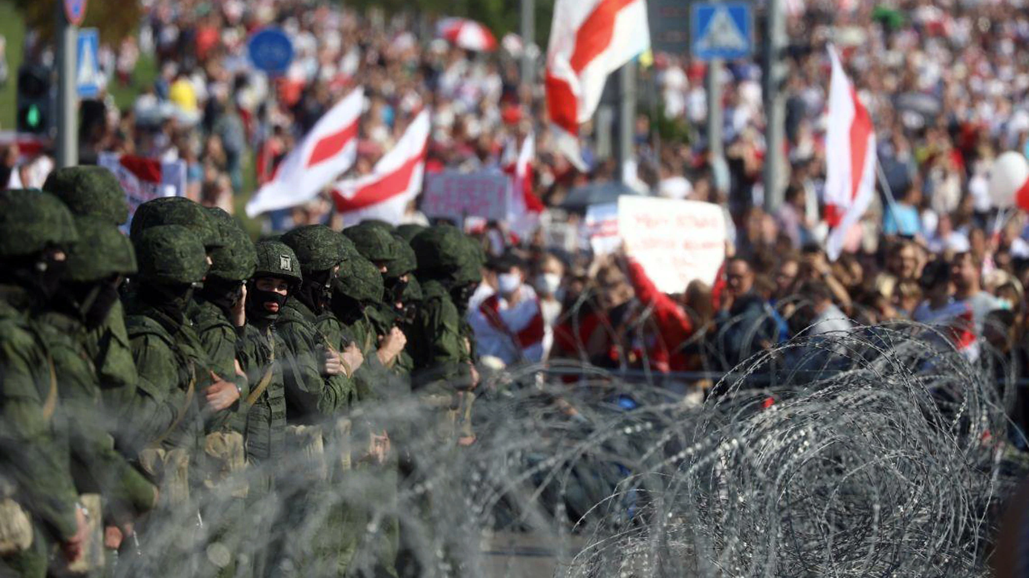 Demonstranten halten die ehemalige belarussische Nationalflagge hoch, während sie durch einen Stacheldrahtzaun an ihrem Protestmarsch gehindert werden sollen.&nbsp;