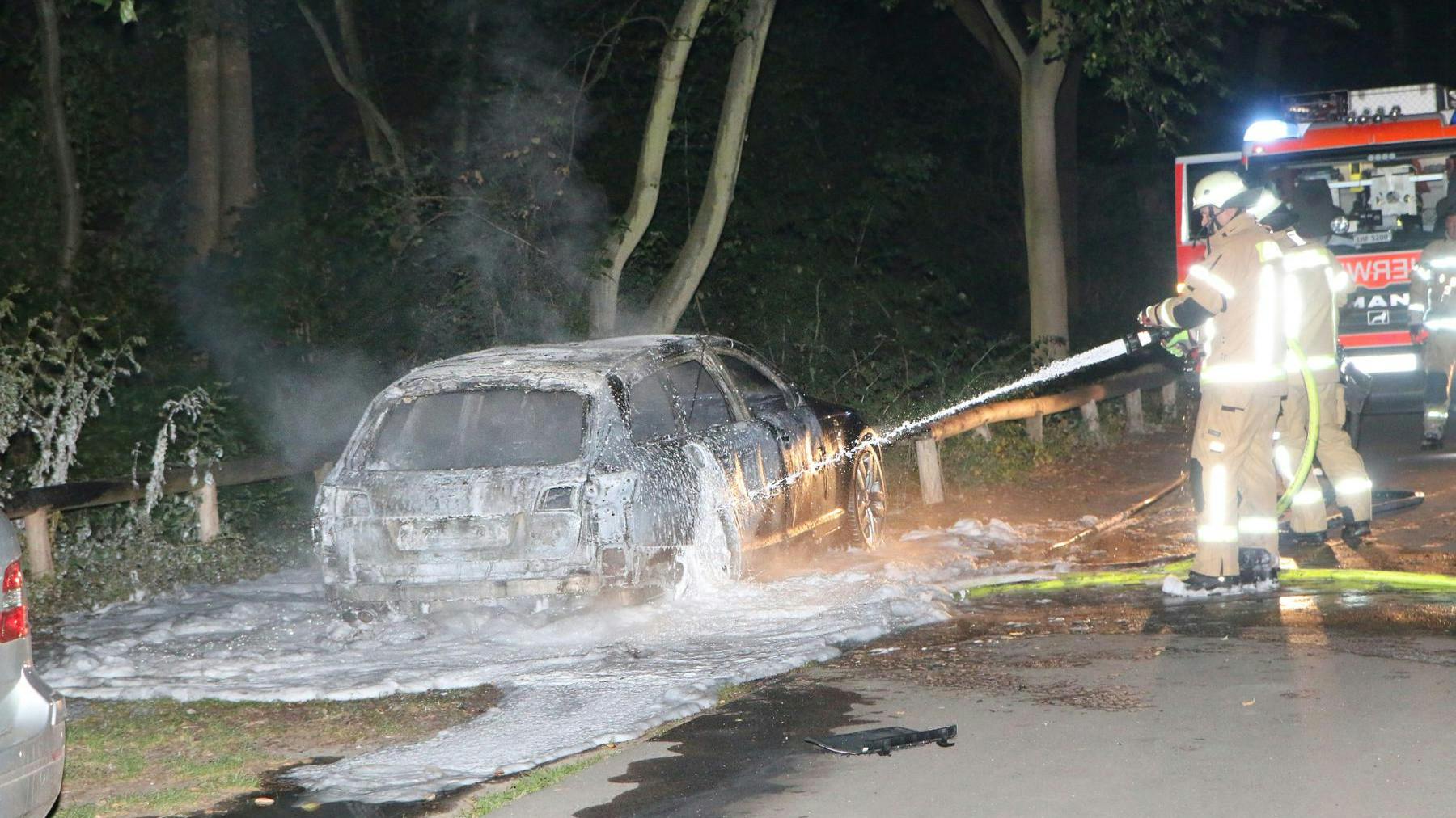 Feuerwehrleute löschen einen schwarzen Audi in Britz. Die Polizei geht davon aus, dass es sich dabei um den Fluchtwagen der Bankräuber handelt.