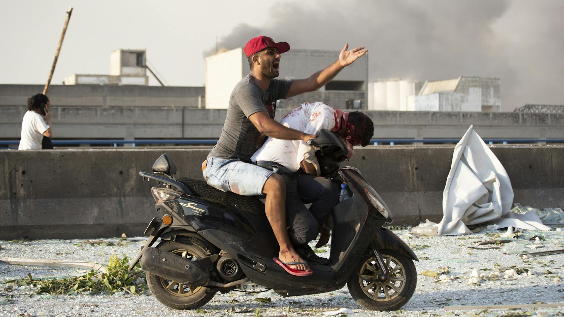 Ein Mann transportiert einen Verletzten auf seinem Motorroller ab.