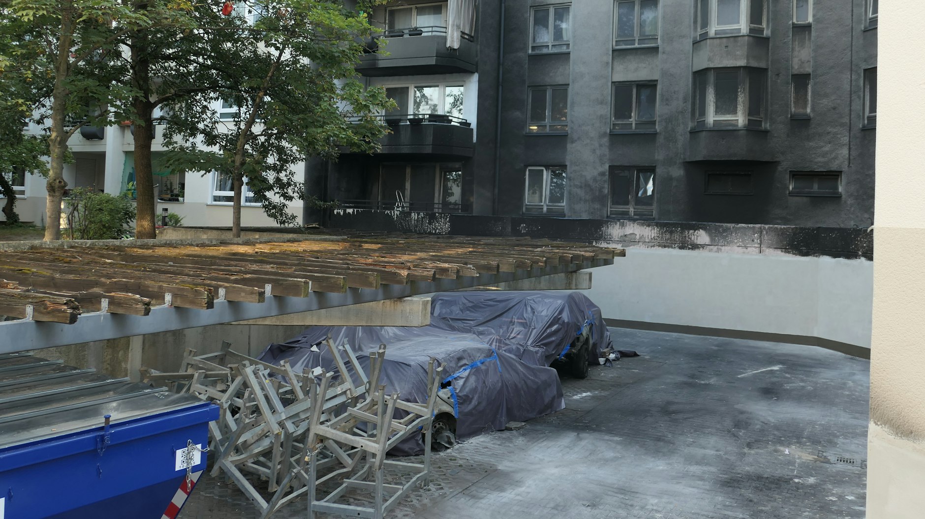 Die Tiefgarage ist zugemauert, das stützt das Haus. Im Vordergrund stehen abgedeckte Autowracks.