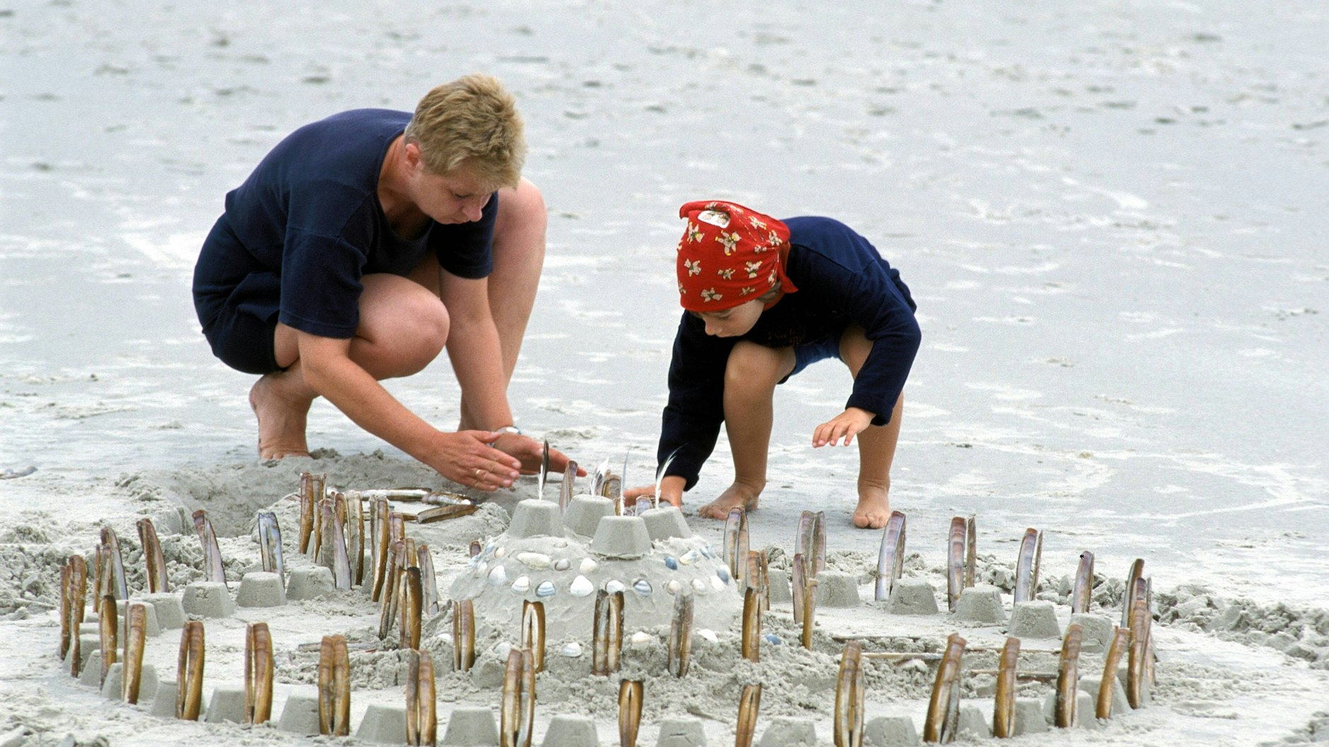 Mutter und Tochter bauen eine Sandburg mit Muscheln.&nbsp;
