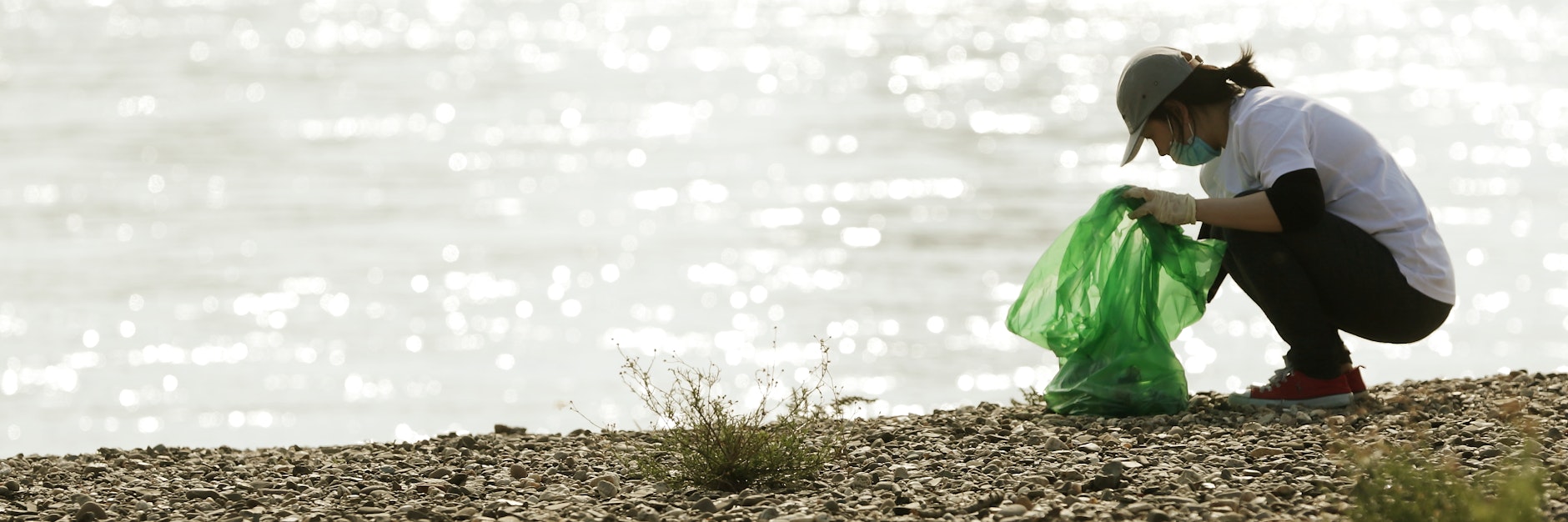 Eine Frau kniet am Rheinufer, um Müll aufzusammeln.