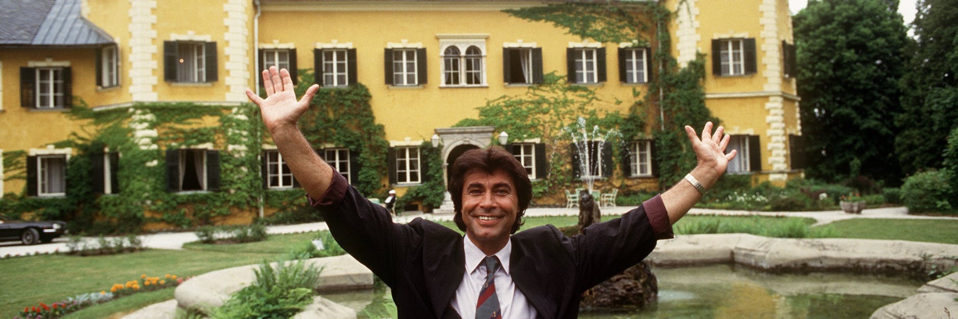 Schlagerstar Roy Black steht mit erhobenen Armen vor dem Schloss am Wörthersee bei Velden in Kärnten, Schauplatz der RTL-Serie „Ein Schloß am Wörthersee“.