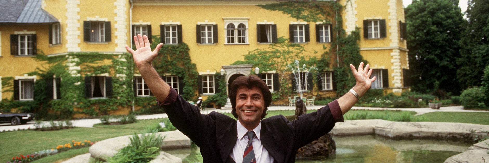 Schlagerstar Roy Black steht mit erhobenen Armen vor dem Schloss am Wörthersee bei Velden in Kärnten, Schauplatz der RTL-Serie „Ein Schloß am Wörthersee“.