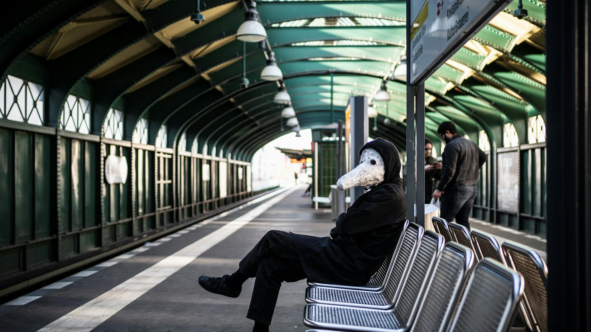 Ein Mann sitzt mit einer Maske im U-Bahnhof Eberswalder Straße, die an die Schnabelmasken in der Zeit der Pest erinnern soll.<br>