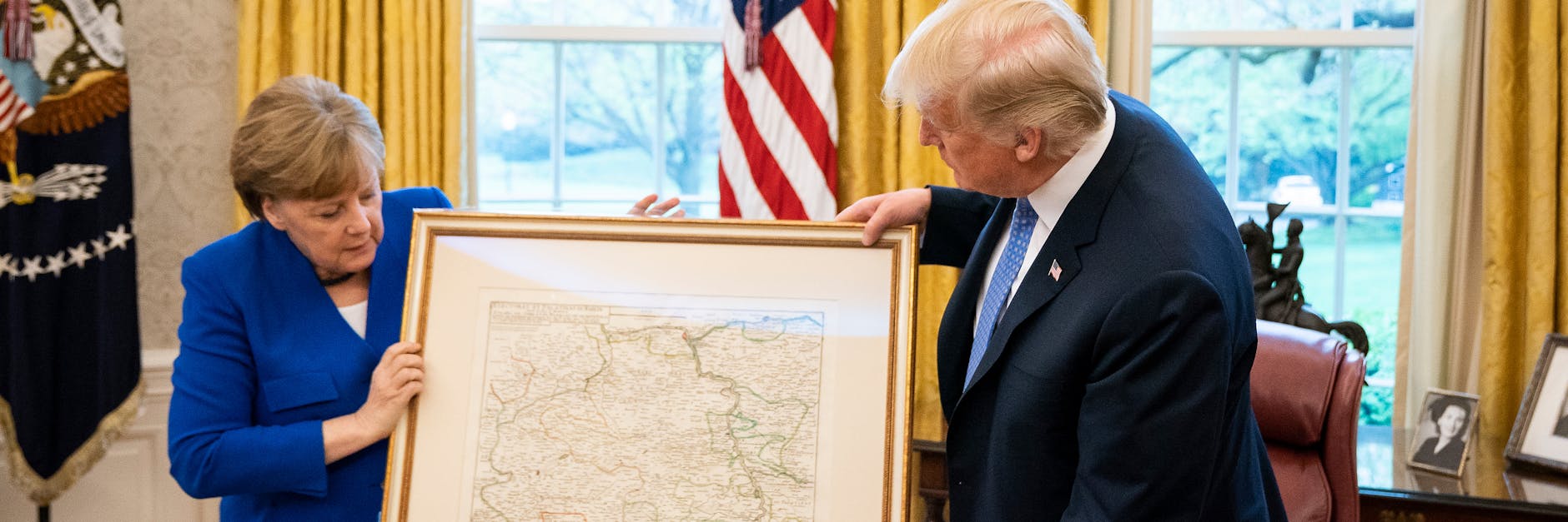 Kanzlerin Angela Merkel (CDU) zeigt US-Präsident Donald Trump auf einer alten Karte, wo sich das Trump-Dorf befindet.