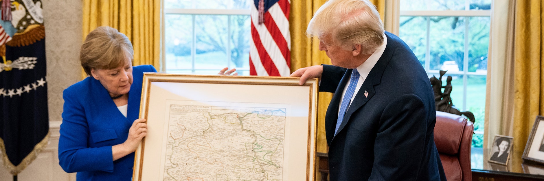 Kanzlerin Angela Merkel (CDU) zeigt US-Präsident Donald Trump auf einer alten Karte, wo sich das Trump-Dorf befindet.