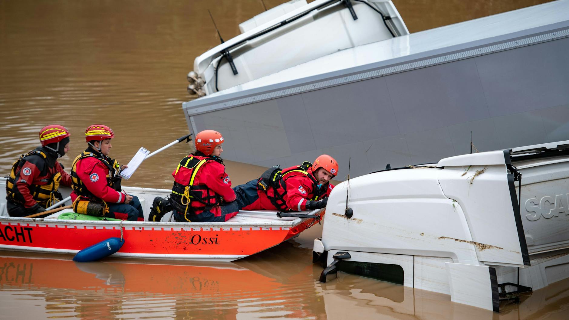 16.07.2021, Nordrhein-Westfalen, Erftstadt: Helfer der Wasserwacht untersuchen von einem Boot aus Lastwagen, die auf der überfluteten Bundesstraße 265 stehen. Foto: Marius Becker/dpa +++ dpa-Bildfunk +++