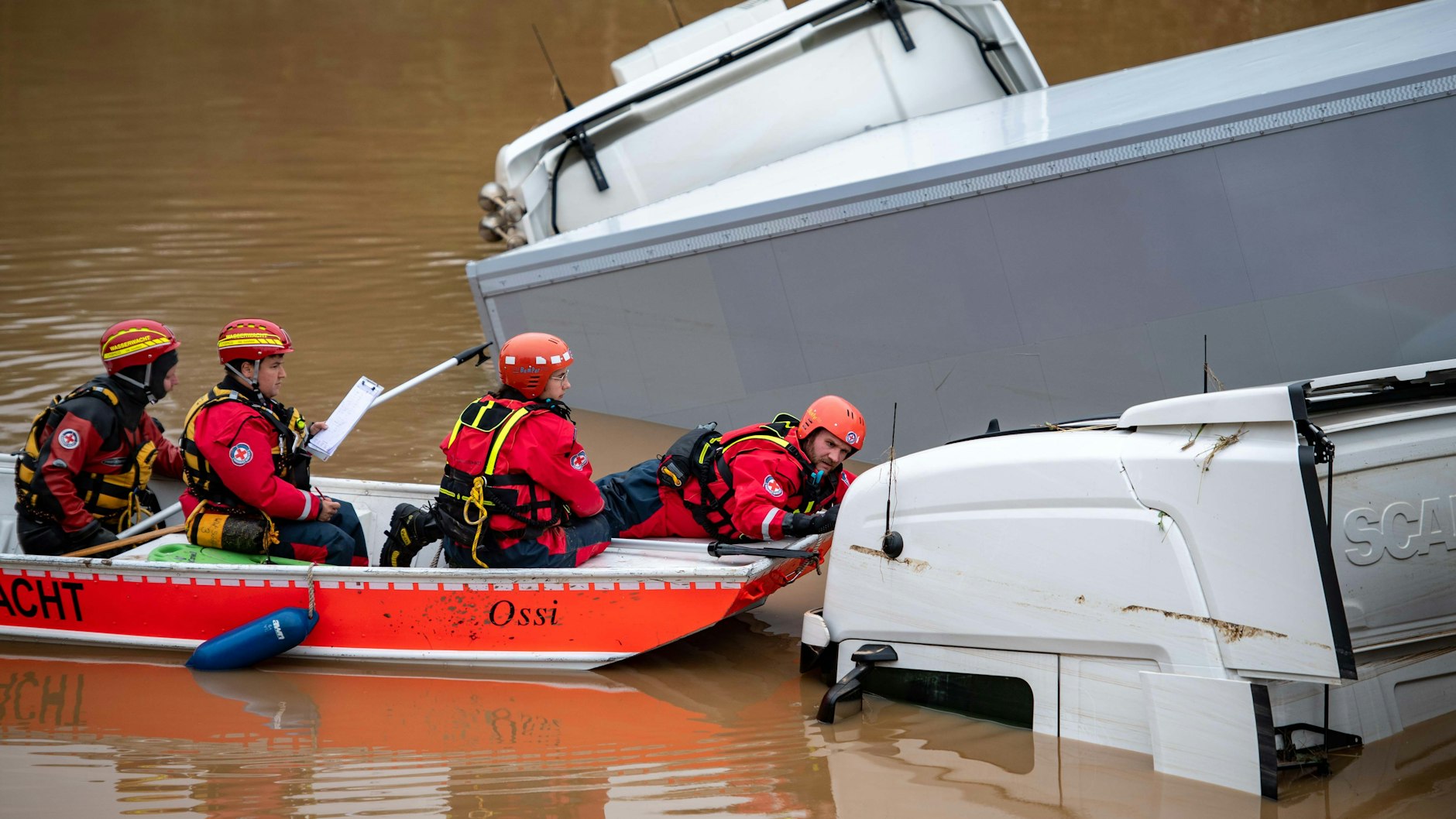 16.07.2021, Nordrhein-Westfalen, Erftstadt: Helfer der Wasserwacht untersuchen von einem Boot aus Lastwagen, die auf der überfluteten Bundesstraße 265 stehen. Foto: Marius Becker/dpa +++ dpa-Bildfunk +++