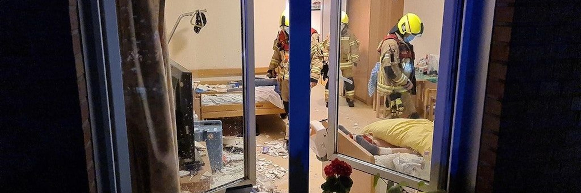 Teile der Zimmerdecke liegen auf dem Boden und den Betten verteilt. Feuerwehrleute tragen bei der Begutachtung des Schadens zur Sicherheit Helme.