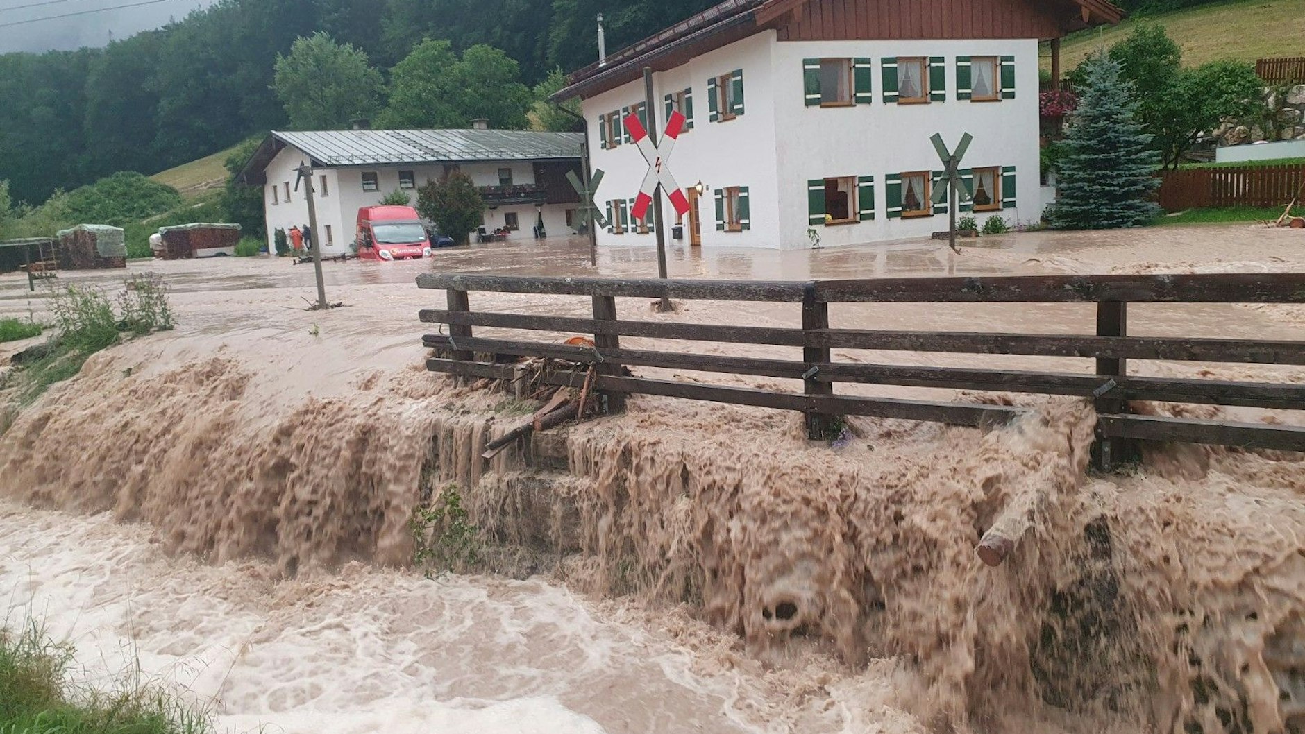 Wasser fließt über einen Platz vor einem Haus im bayerischen Bischofswiesen. Der Landkreis Berchtesgadener Land hat nach starkem Regen wegen Hochwassers den Katastrophenfall ausgerufen.