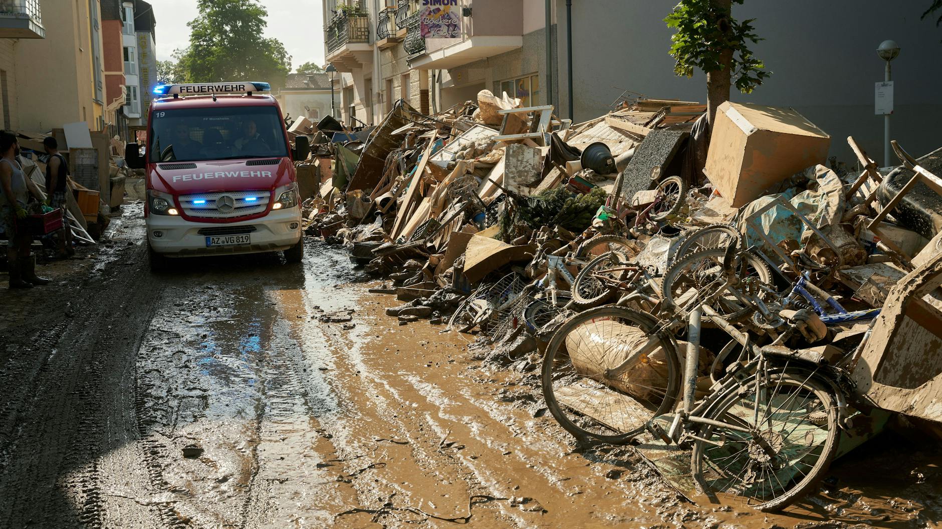 Ein Einsatzwagen der Feuerwehr fährt durch eine Straße in Bad Neuenahr, die mit Sperrmüll gesäumt ist.