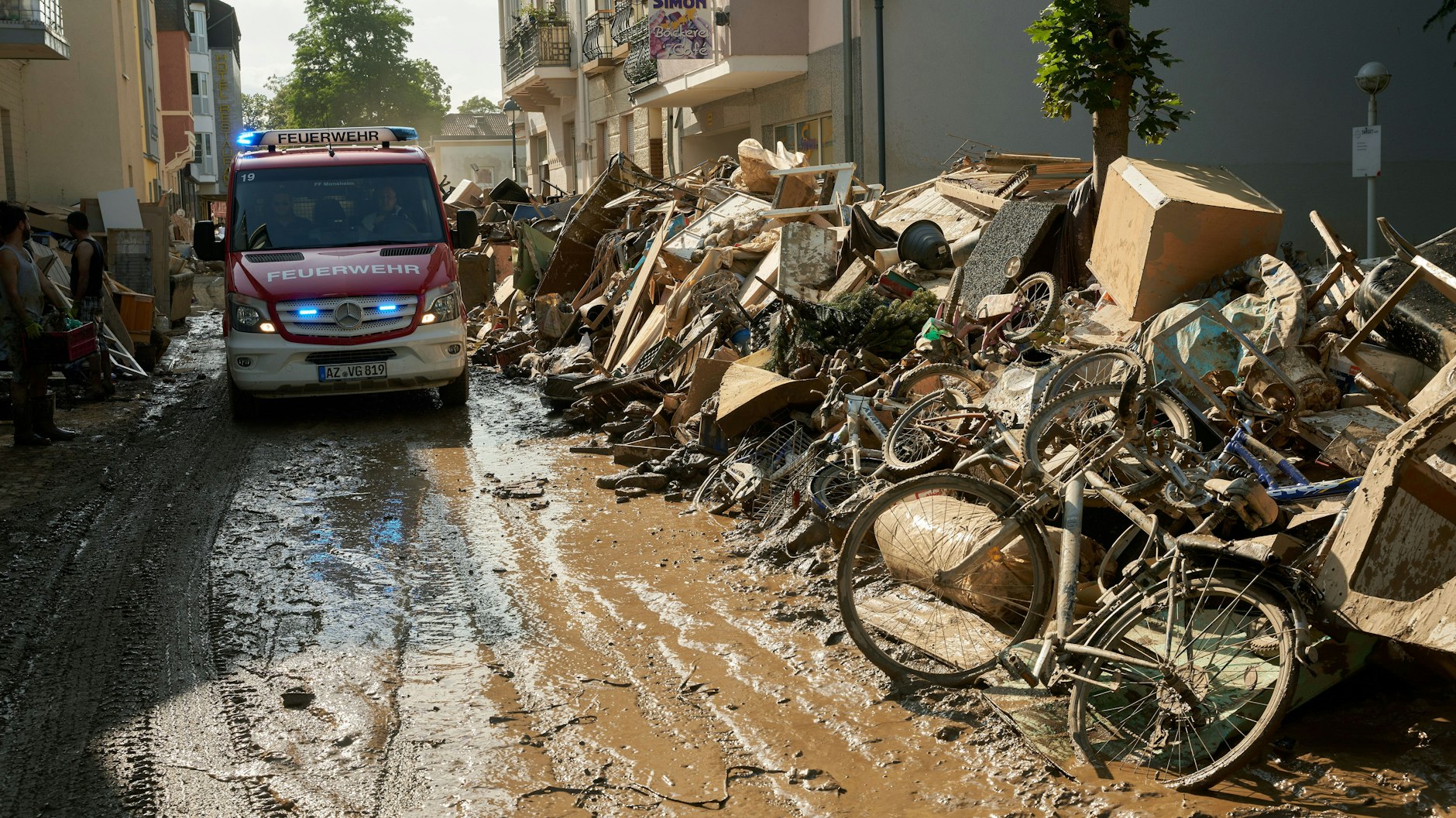 Ein Einsatzwagen der Feuerwehr fährt durch eine Straße in Bad Neuenahr, die mit Sperrmüll gesäumt ist.