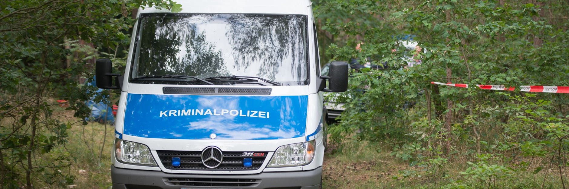 Ein Wagen der Kriminalpolizei steht in einem Wald nahe des Tatorts.