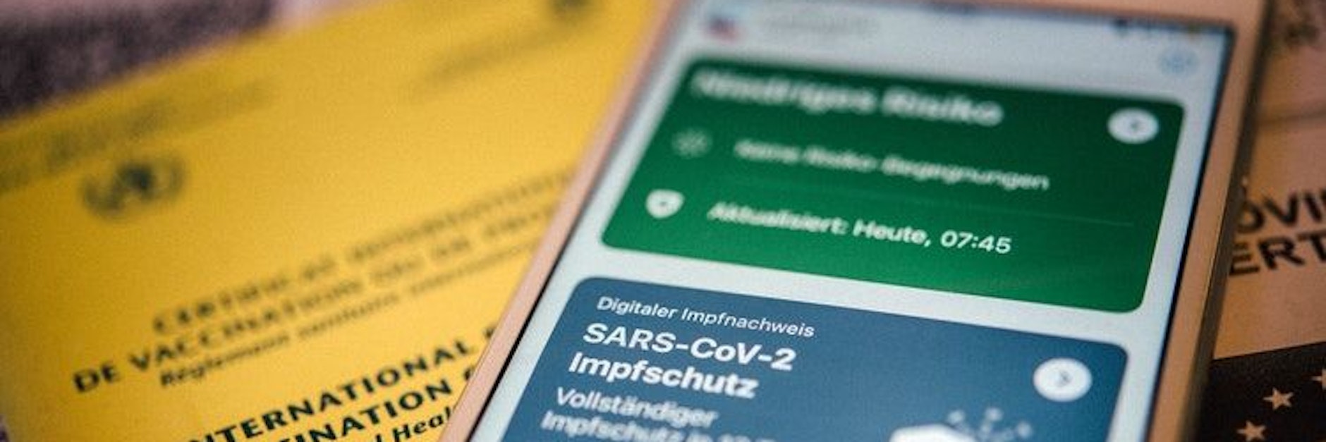 Ein gelber Impfausweis und der digitale Impfpass in der Corona-Warn-App