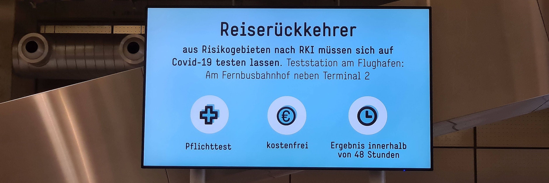 Ein Schild weist Reiserückkehrer auf die Regeln am Flughafen hin.