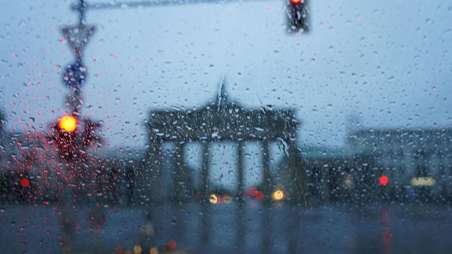 Durch eine mit Regentropfen bedeckte Scheibe eines Autos ist das Brandenburger Tor in Berlin zu sehen.