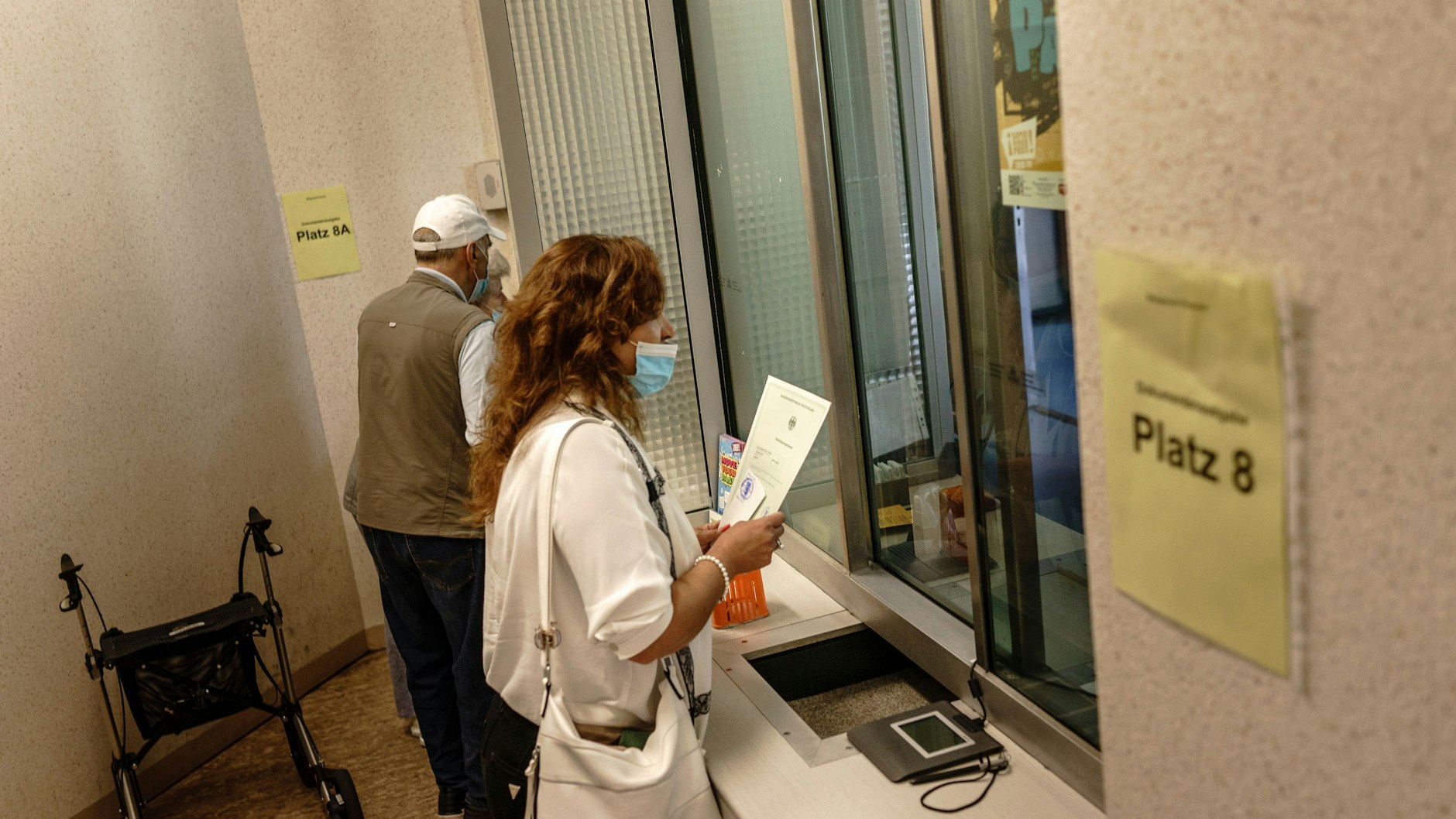 Mit der frischen Einbürgerungsurkunde steht eine Frau vor einem Schalter, um ihren deutschen Pass zu beantragen.<br>