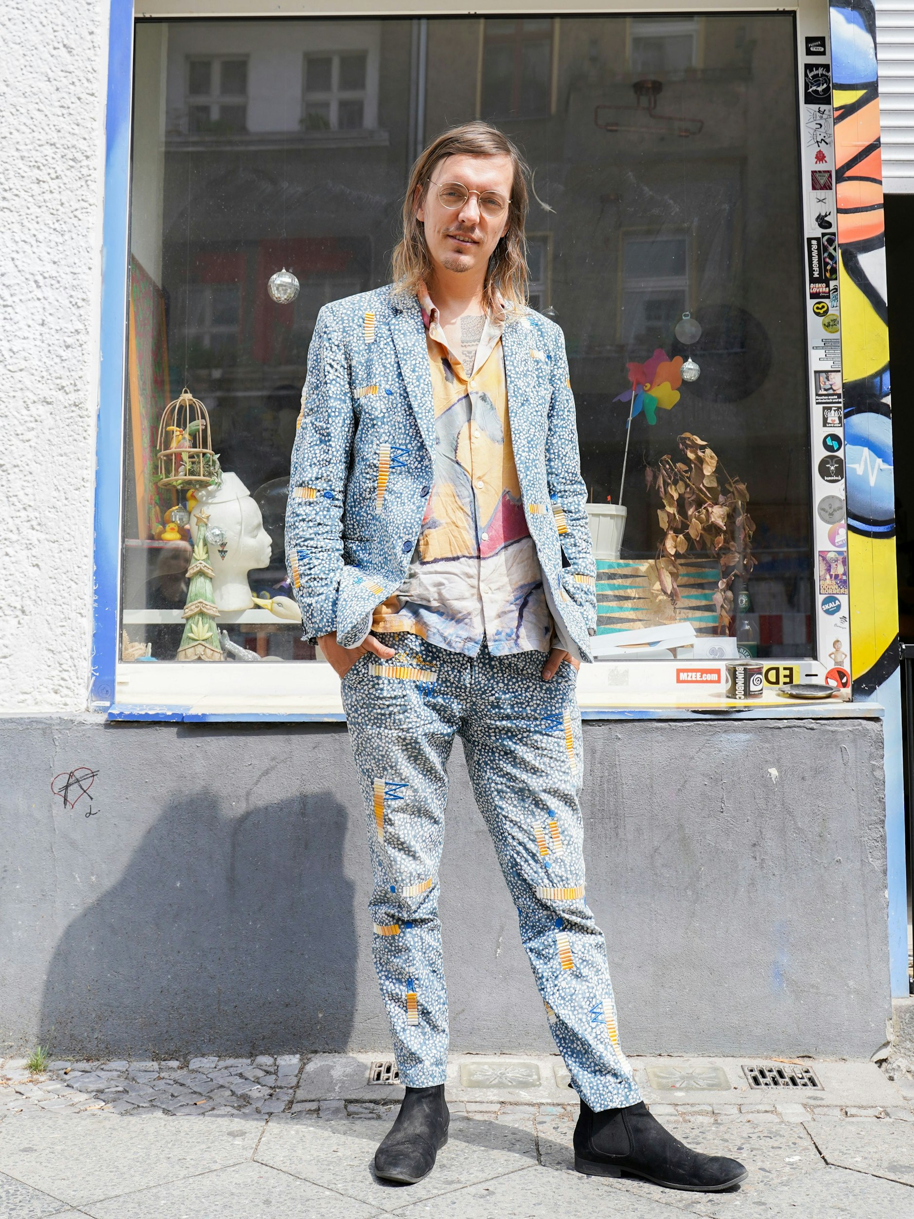 Ole ist visueller Künstler und Modemacher. Der gebürtige Berliner lebt die meiste Zeit in Ubud auf Bali, wo er gerade eine kleine Wohnanlage für Künstler aufbaut. Er hat einen Anzug aus seiner eigenen Kollektion an, dazu trägt er ein selbst gemachtes Hemd mit Kandinsky-Print und italienische Chelsea Boots.