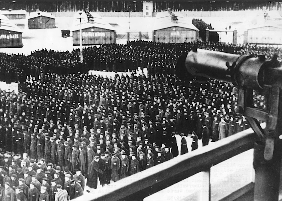 Häftlinge sind im KZ Sachsenhausen angetreten, ein Maschinengewehr ist auf sie gerichtet. Ein jetzt 100 Jahre alter Mann war in dem Lager, in dem mehrere 10.000 Menschen ihr Leben ließen, Wachmann.&nbsp;