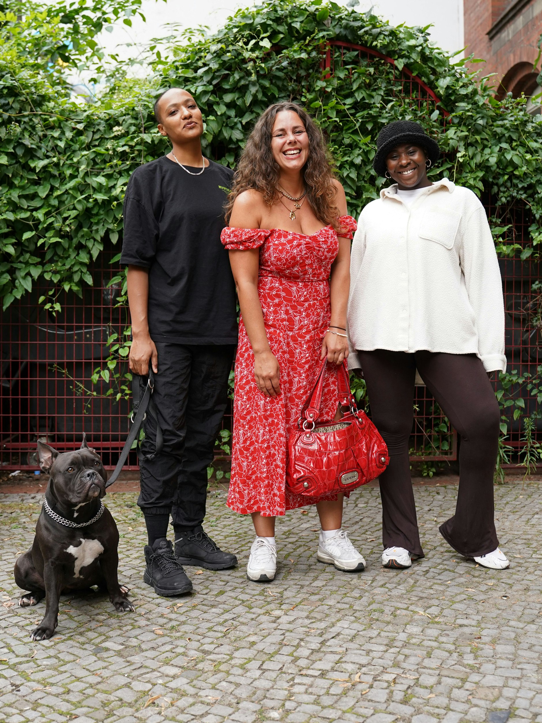 Die Musikerin Nuria, die Eventkuratorin Andra und die Tänzerin Gifty sind Freundinnen. Die ganz in Schwarz gekleidete Nuria (Shirt von Bershka, Iriedaily-Hose und Timberland-Sneakers) passt gerade auf die Bulldogge Chili auf, die eigentlich der Berliner Rapperin Nura gehört. Andra trägt ihr Traumkleid von Andotherstories zu Nike Sneakers und eine Vintage-Tasche von Guess; Gifty eine weiße Weekday-Jacke, Asos-Hose und Asics-Sneakers.