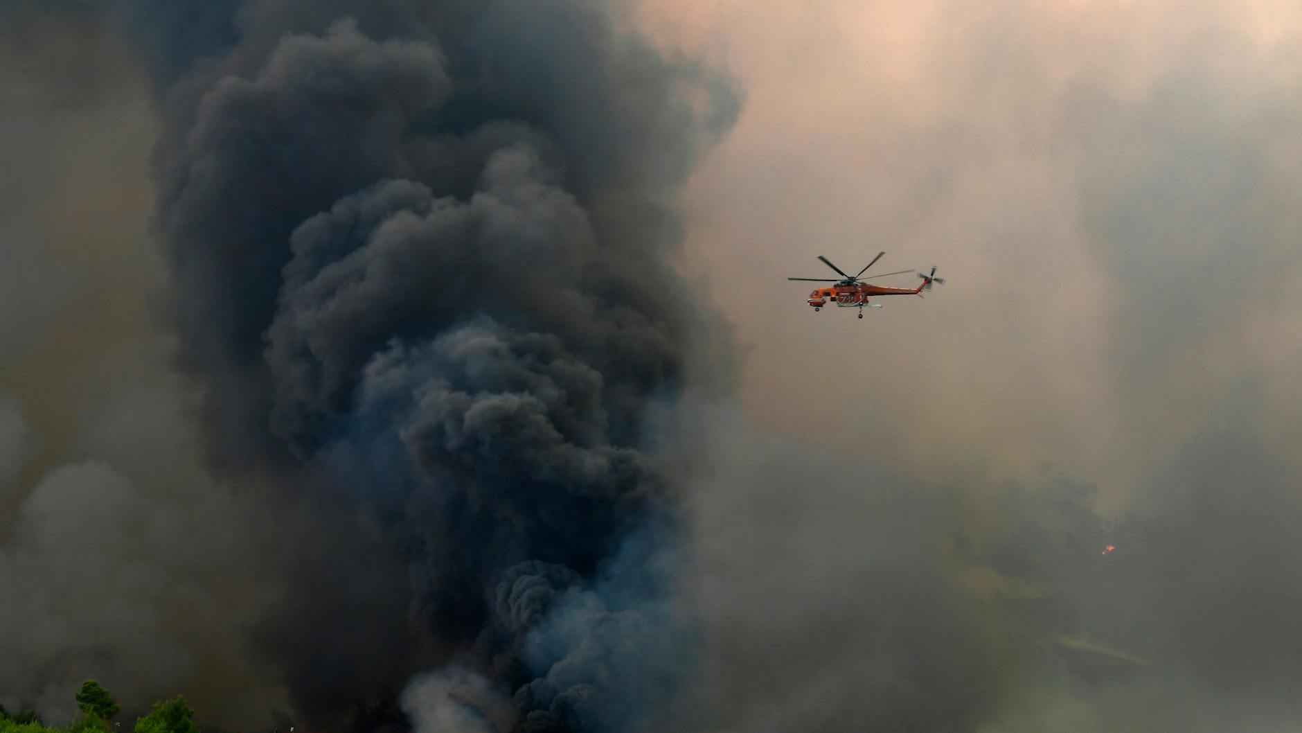 Ein Hubschrauber fliegt über einem Waldbrand im Norden von Athen.