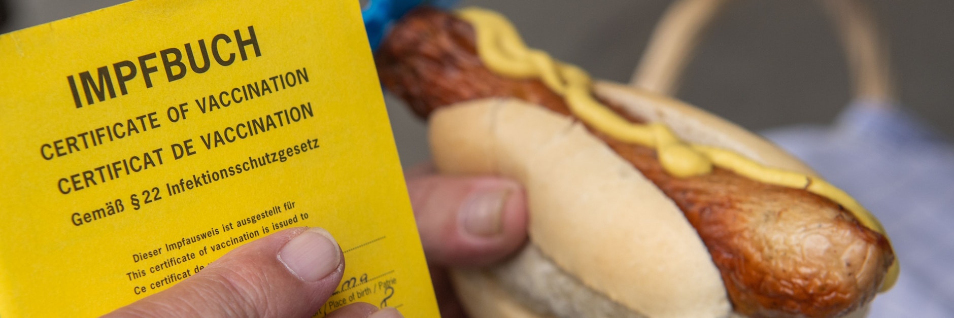 Ein Mann hält nach seiner Impfung gegen das Coronavirus eine Bratwurst in der Hand.