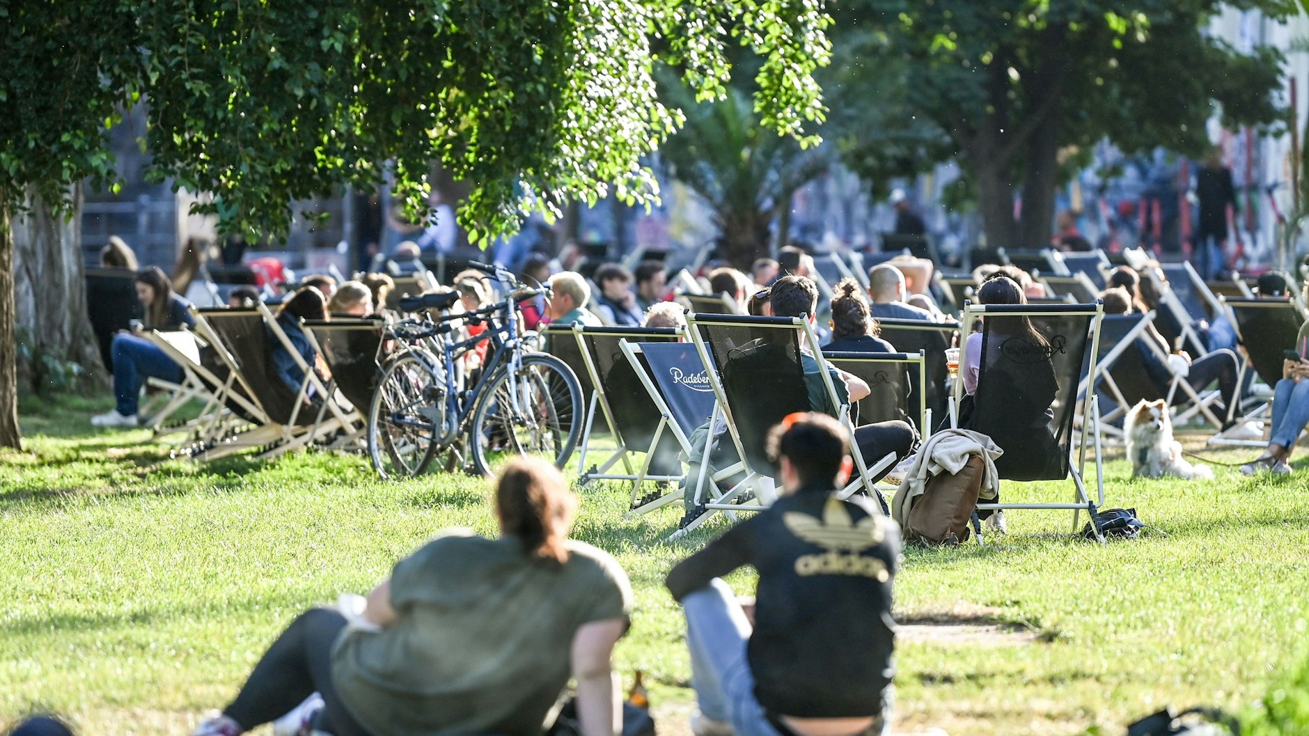 Zahlreiche Menschen sitzen auf Liegestühlen und auf der Wiese in der untergehenden Sonne am Sonntagabend im James-Simon-Park. In Berlin ist die Sieben-Tage-Inzidenz weiter gestiegen.