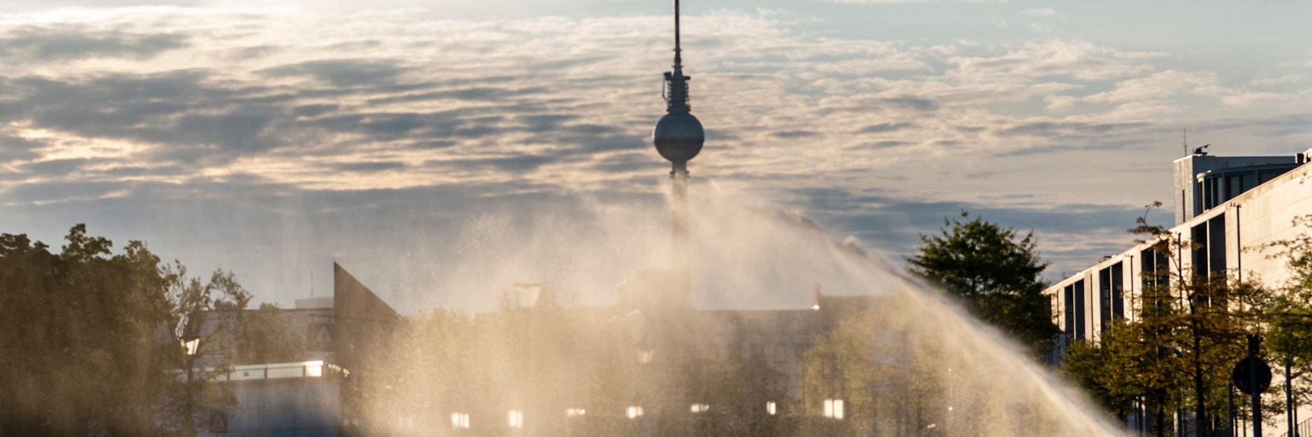 Es wird wieder glutheiß: Das Wasser eines Rasensprengers berieselt im Gegenlicht der Sonne im Regierungsviertel eine Rasenfläche und Bäume. 