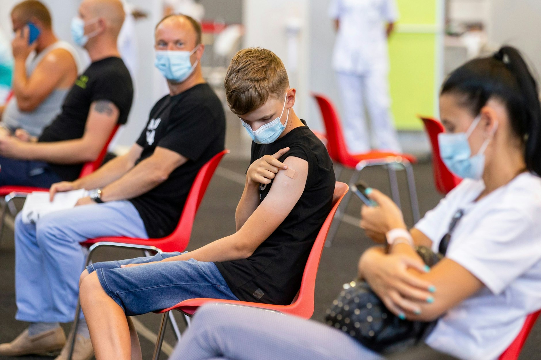 Ein Zwölfjähriger (Mitte) und sein Vater (links von ihm) sitzen im Wartebereich, nachdem sie gegen das Coronavirus geimpft worden sind.