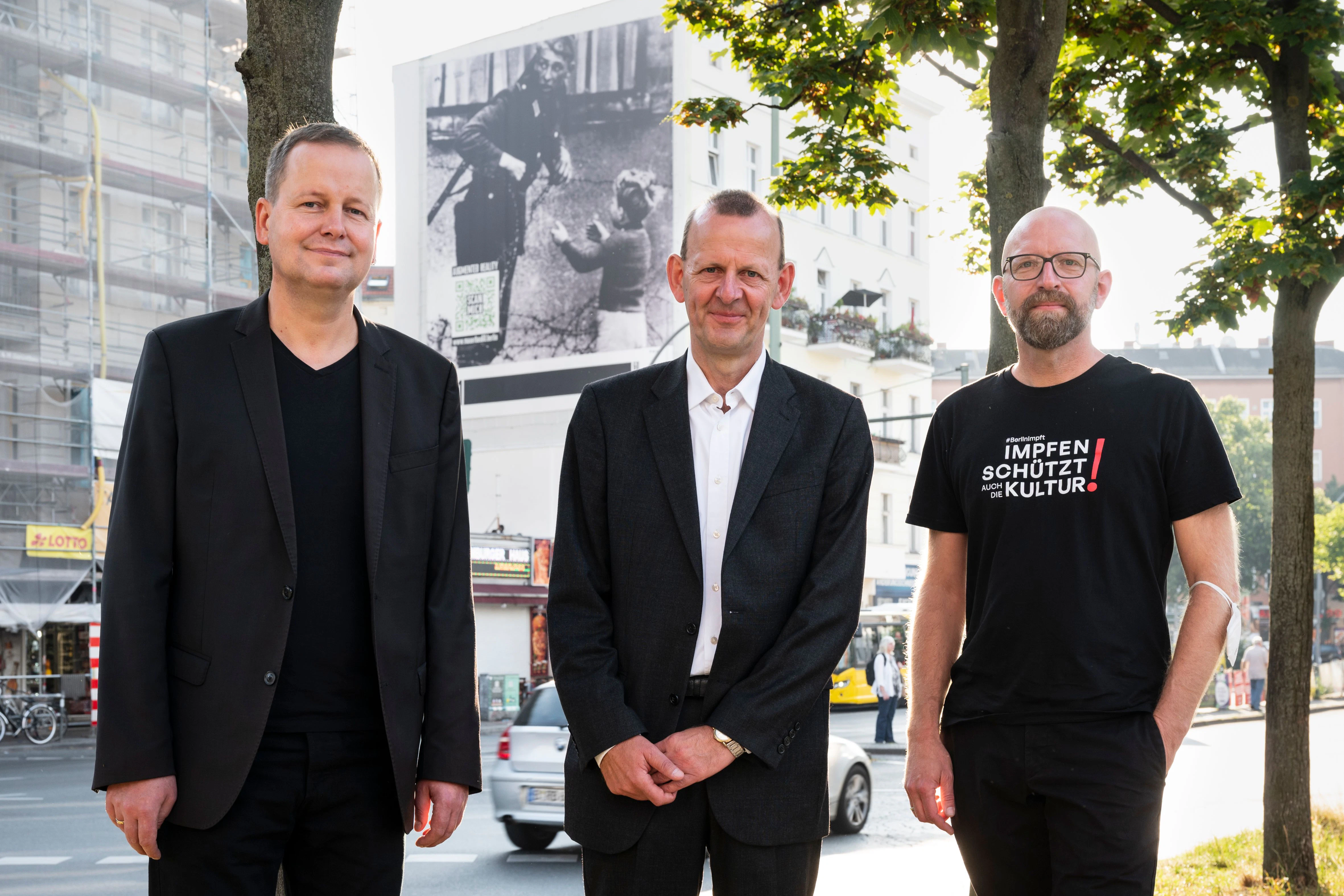 Klaus Lederer, Axel Klausmeier und Moritz van Dülmen (v.l.) vor dem Plakat am Hermannplatz.