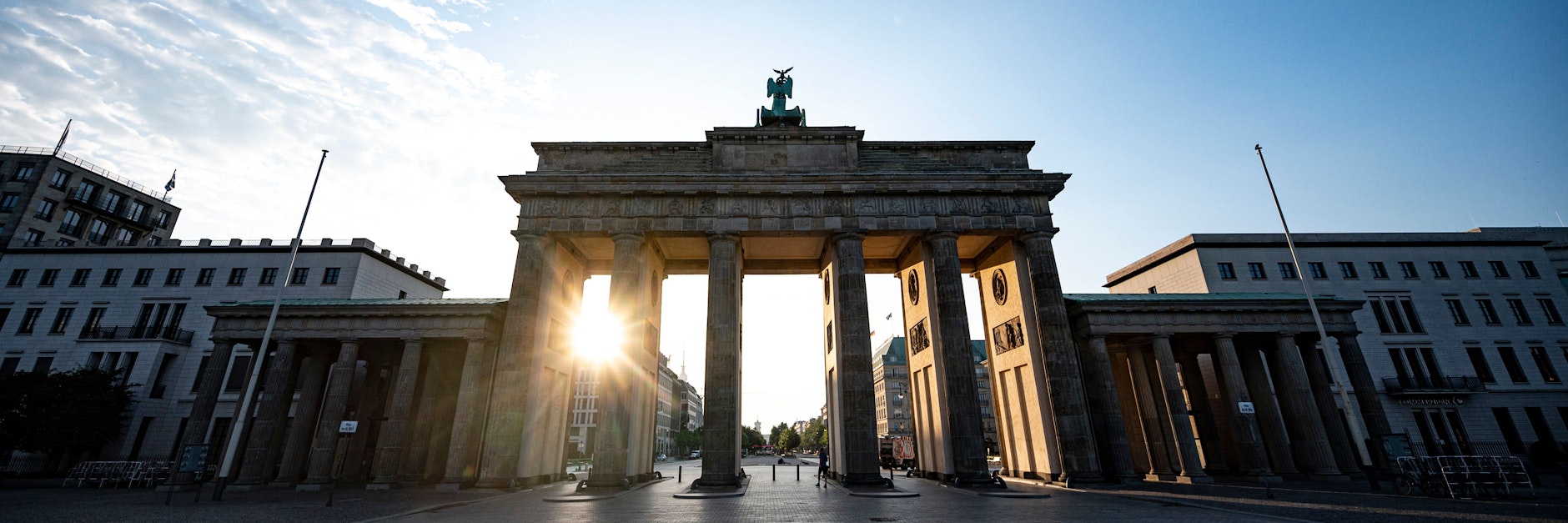 Die aufgehende Sonne scheint durchs Brandenburger Tor. Es wird ein schönes Sommerwochenende in Berlin.
