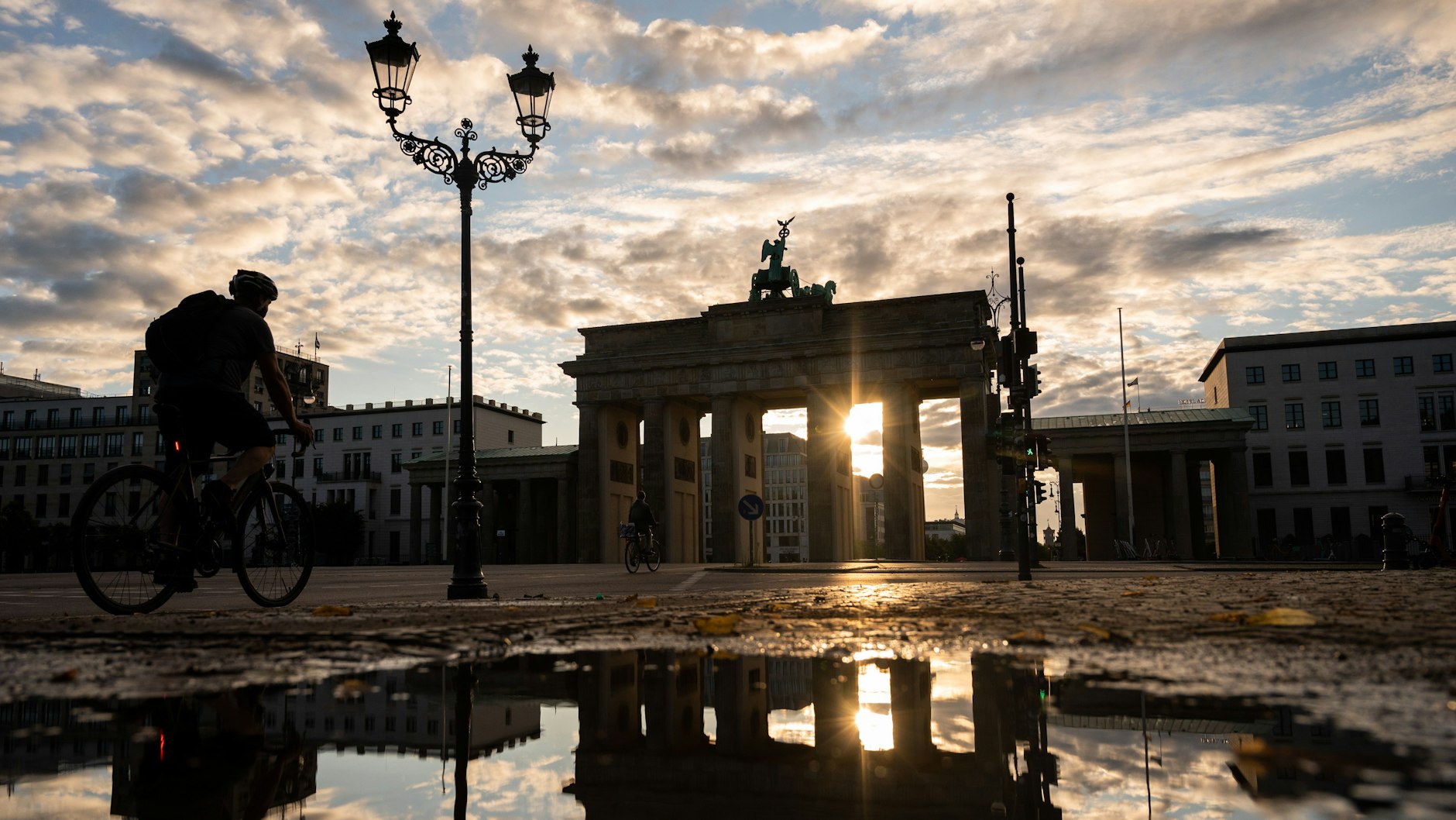 Das Brandenburger Tor spiegelt sich während des Sonnenaufgangs in einer Pfütze.
