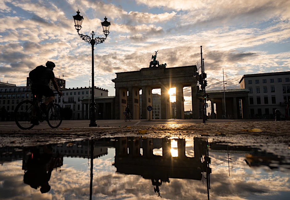 Das Brandenburger Tor spiegelt sich während des Sonnenaufgangs in einer Pfütze.