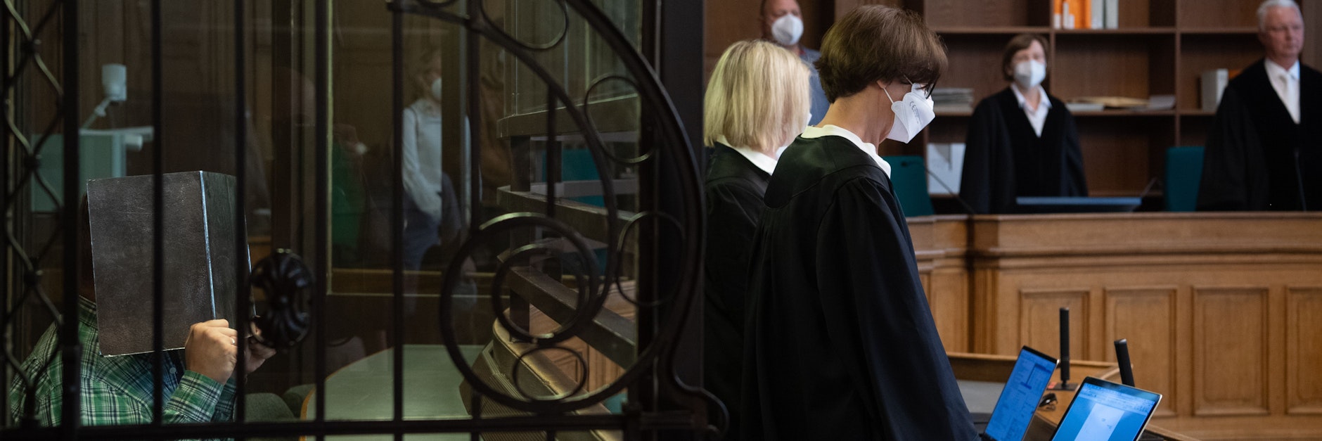 Der Angeklagte (l) sitzt in einem Gerichtssaal und hält sich eine Pappe vor dem Gesicht. Der 41 Jahre alte Lehrer muss sich wegen mutmaßlichem Mord verantworten. Der Beschuldigte soll einen 43-jährigen Mann, den er kurz zuvor über ein Dating-Portal kennengelernt hatte, in seiner Wohnung getötet haben.